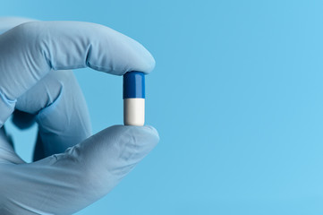 Close-up shot of capsule pill in nurse's hand on blue background. A female hand in a medical glove is holding an antiviral capsule. Prevent pandemic spread. Copy space. 