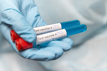 Obraz premium Coronavirus vaccine, positive and negative. Doctor in protective suit, medical mask and latex gloves holds a test tubes with vaccine. 