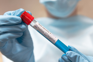 Coronavirus vaccine, positive. Doctor in protective suit, medical mask and latex gloves holds a test tube with vaccine. 