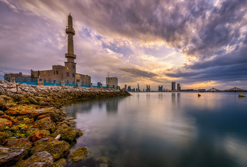 Fototapeta na wymiar Beautiful view of Hanan Ali Kanoo Mosque in Al Ghous park and Manama city at the background with striking clouds during sunset.