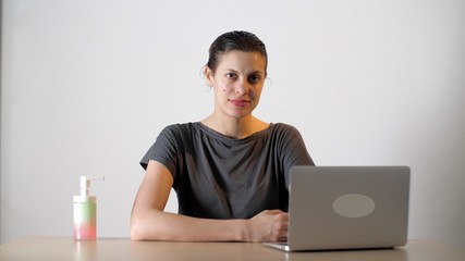 Woman sitting at the table with a laptop. Nearby is a liquid soap or sanitizer. Pandemic and quarantine is over. Recovery. Coronavirus or Covid-19.