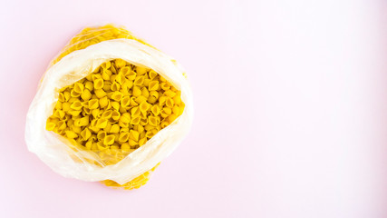 Macaroni in a bag in the form of shells with additives on a pink background.