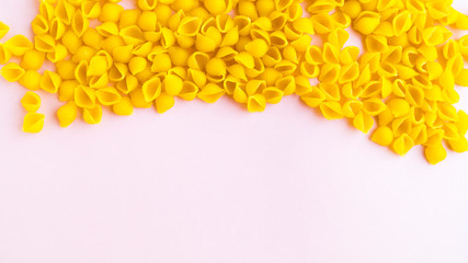 Sprinkled pasta in the form of shells with additives on a pink background.