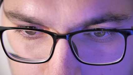 Close-up face of a male eyes with glasses works at the computer. Display reflection in glasses. Portrait of a young man programmer  with glasses. Work in home. Quarantine