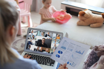 Young woman works from home with child at the background during self isolation and quarantine. Work...