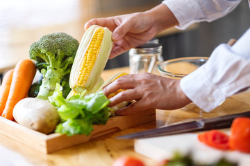 A woman chef holding and picking a fresh corn from a vegetables tray on the table
