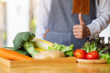 Closeup image of a female chef making and showing thumbs up hand sign while preparing fresh mixed vegetables to cook in kitchen