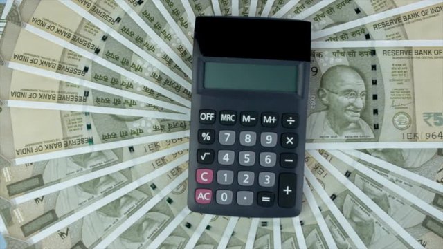 Top view shot of a calculator and five hundred rupees notes - accounting concept. Closeup shot of 500 Indian currency notes revolving on a turntable with a calculator against the blue platform