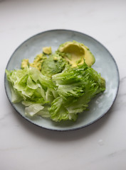 lettuce and avocado in rustic plate on white marble background