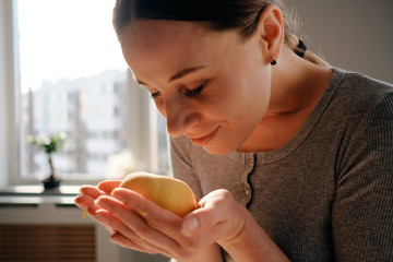 Portrait happy woman holding dough in hands while smelling it with a window in the background