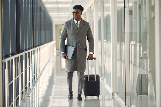 Black man at the airport. Guy with suitcase. Male in a black suit.