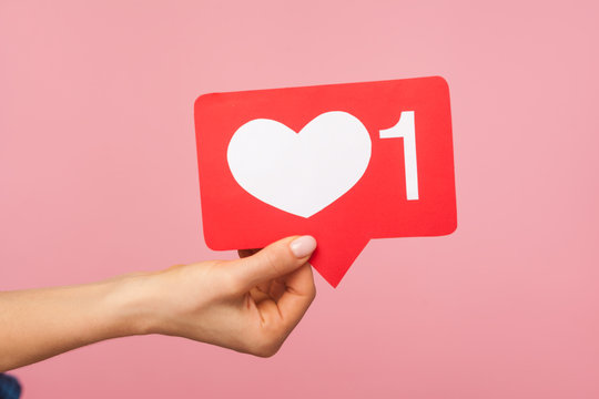 Closeup of hand holding social media heart like icon with number one, recommendation to support trendy interesting content, subscribe and follow blog. indoor studio shot isolated on pink background - Powered by Adobe
