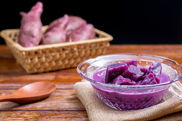 Purple sweet potato with coconut milk in transparent bowl on wooden table on black background. Delicious Thai dessert.