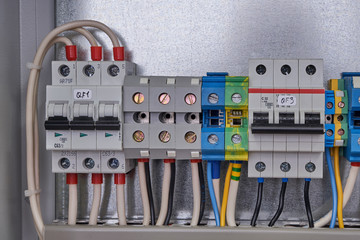 Two modular electrical circuit breakers and terminals with connected wires in the electrical Cabinet. Grey terminals for connecting phases. Blue neutral terminals. Yellow-green earth terminals.