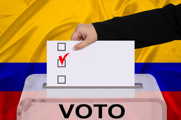 female voter drops a ballot in a transparent ballot box against the backdrop of the Colombia national flag, concept of state elections, referendum