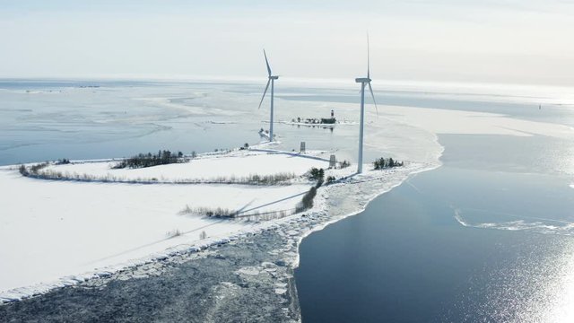 Flying around two windmills standing at the coast of Baltic sea with lighthouse and floating ice floes, Holmsund locality, close to Umea city, Vasterbotten county, Sunny spring day