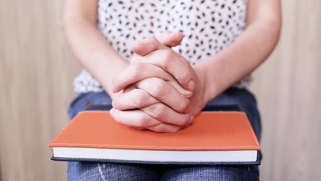 Close-up. Arms. Woman in jeans crosses her fingers on a diary.