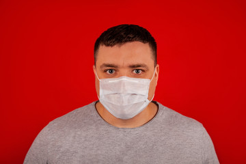 Portrait of a young man looking at the camera in a medical protective mask on a red background