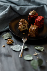a piece of sliced cupcake in colored chocolate glaze served on a black plate a stylish composition with walnuts