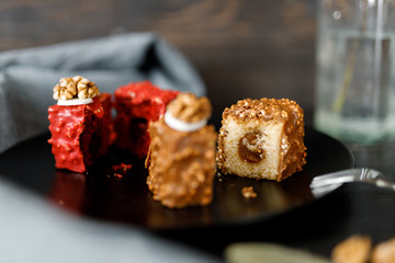 a piece of sliced cupcake in colored chocolate glaze served on a black plate a stylish composition with walnuts