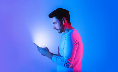 Glow of phone in hands of guy with wireless headphones - obrazy, fototapety, plakaty