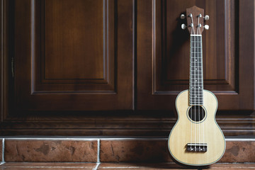 Standing ukulele leaning against wooden cabinet
