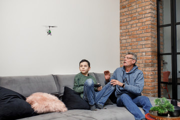 Happy family, old grandfather and cute little boy grandson play  toy plane lay on sofa, funny small...