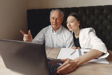 Senior with a young assistant. Businessman working in the cafe. Man in a white shirt. Young woman with her boss.