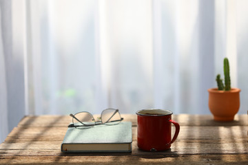 Red coffee cup and glasses with green notebook and cactus pot on rustic wooden table 