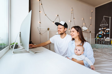Parents With Baby Working At Home Looking At Computer