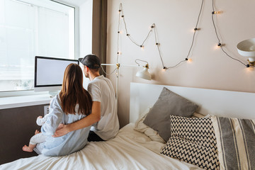 Parents With Baby Working At Home Looking At Computer
