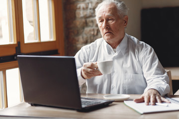 Senior with a laptop. Businessman working in the cafe. Man in a white shirt.