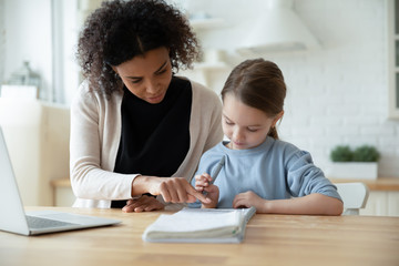 Caring African American mom help little Caucasian daughter studying together online at home, biracial mother teach learn with European girl child, have internet web class, homeschooling concept