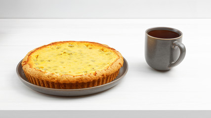 Homemade gooseberry pie with yogurt filling and cup of tea on white wooden table.