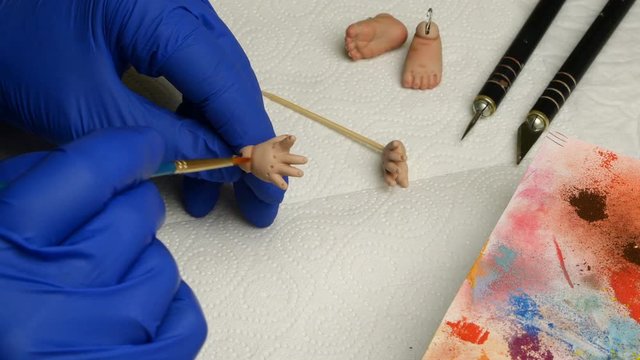 Making dolls. Master puppet intently paints fingers on dolls hand with thin brush. Concept of creating handmade dolls. Close-up.