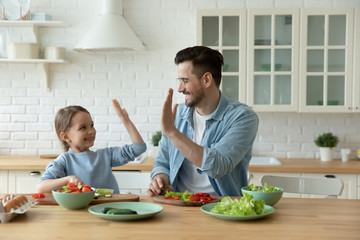 Excited young Caucasian father and little daughter give high five engaged in funny activity cooking...