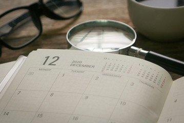 Selective focus monthly planner in page December together with a cup of coffee,magnifying glass and glasses. December represent Q4 or quarter four in business.