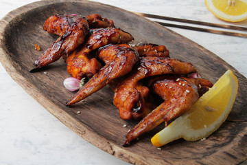 
BBQ chicken wings on a wooden plate with lemon and sesame seeds.