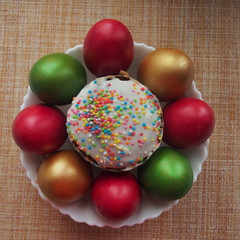 Easter cake and colorful Easter eggs in a white porcelain plate. Raspberry, green and Golden eggs.