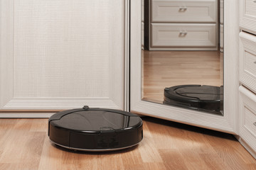 reflection of black robotic vacuum cleaner running on laminate floor before mirror in bedroom. modern smart appliance for cleaning house