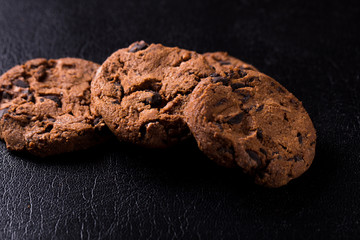 Appetizing chocolate chip cookies with slices of raisins on a black background.