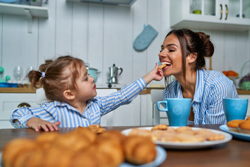 Little daughter feeds her mother with sweet cookies. Family having fun in the kitchen during...