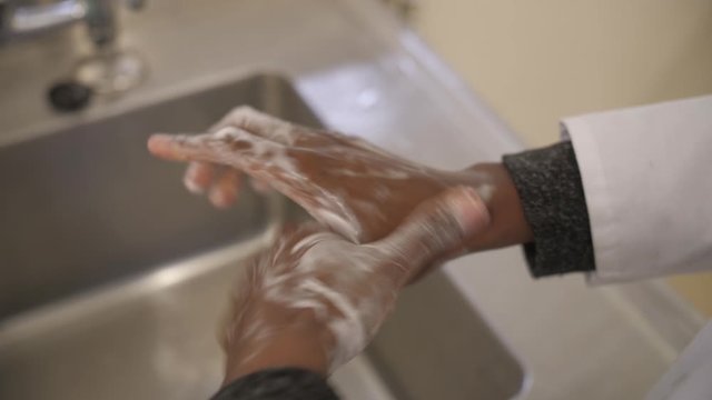 Proper hand washing technique, step 6: Washing of thumbs by clasping and rotating in the palm of the opposite hand. Close up shot, African female washes her hands with soap. Sterile environment.