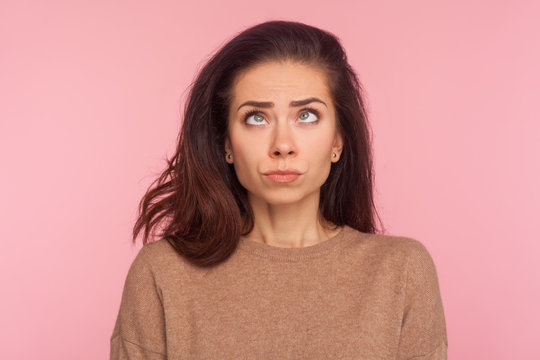 Portrait Of Awkward Funny Young Woman With Brunette Hair Making Silly Comical Face With Eyes Crossed, Thinking Intensely Looking Dumb And Confused. Indoor Studio Shot Isolated On Pink Background