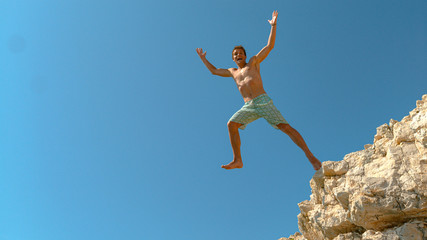 Cinematic shot of a happy Caucasian male tourist cliff diving during his holiday