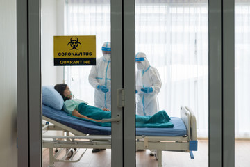 two doctor in personal pretective equipment or ppe treating the asian woman patient with covid-19 or coronavirus infection in the isolation unit in the hospital during pandemic. medical concept - obrazy, fototapety, plakaty