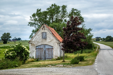 Obraz premium Old weathered brick shed with plaster peeling off next to a small country road in Valleberga, Skane, Southern Sweden.
