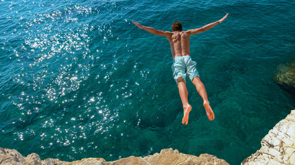 COPY SPACE: Young man on a summer vacation does cliff diving on a sunny day. - obrazy, fototapety, plakaty