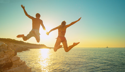 LENS FLARE: Woman holds boyfriends hand as the jump off a cliff and into sea.