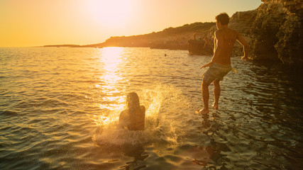 LENS FLARE: Young couple jumps into Mediterranean sea on a sunny summer evening